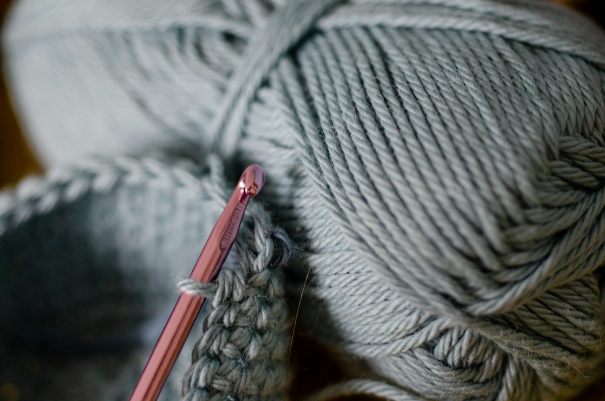 A pink crochet hook beside grey yarn and a close-up of crochet fabric