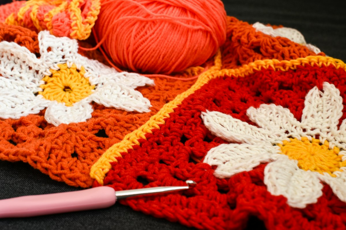 Red and orange crochet squares with white flowers beside yarn and a crochet hook