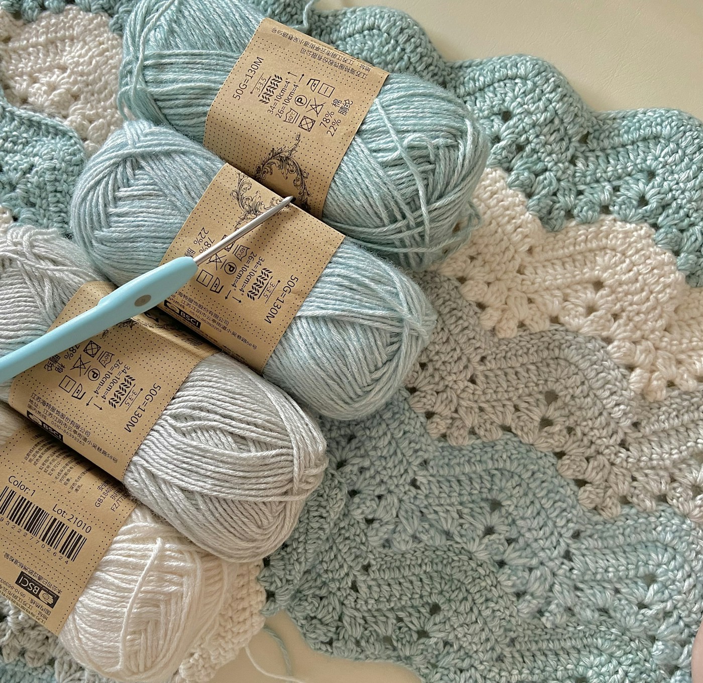 Blue and cream yarn with a crochet hook resting on a textured crochet blanket